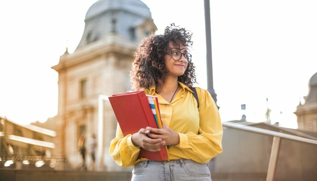 Student holding a folder and standing on the steps outside